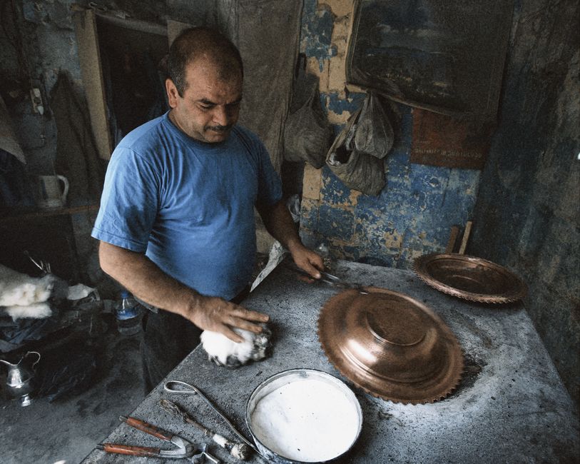 A skilled artisan polishes a copper tray in a traditional workshop, showcasing craftsmanship.